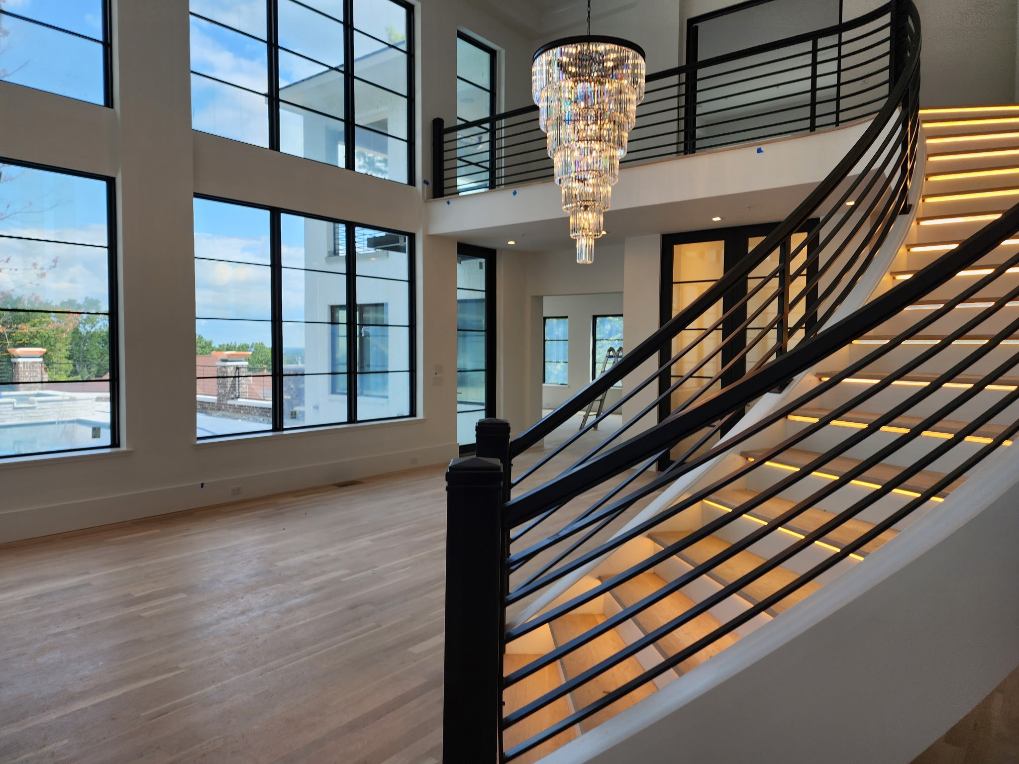 Custom interior with a curved illuminated staircase, black railings, and floor-to-ceiling windows