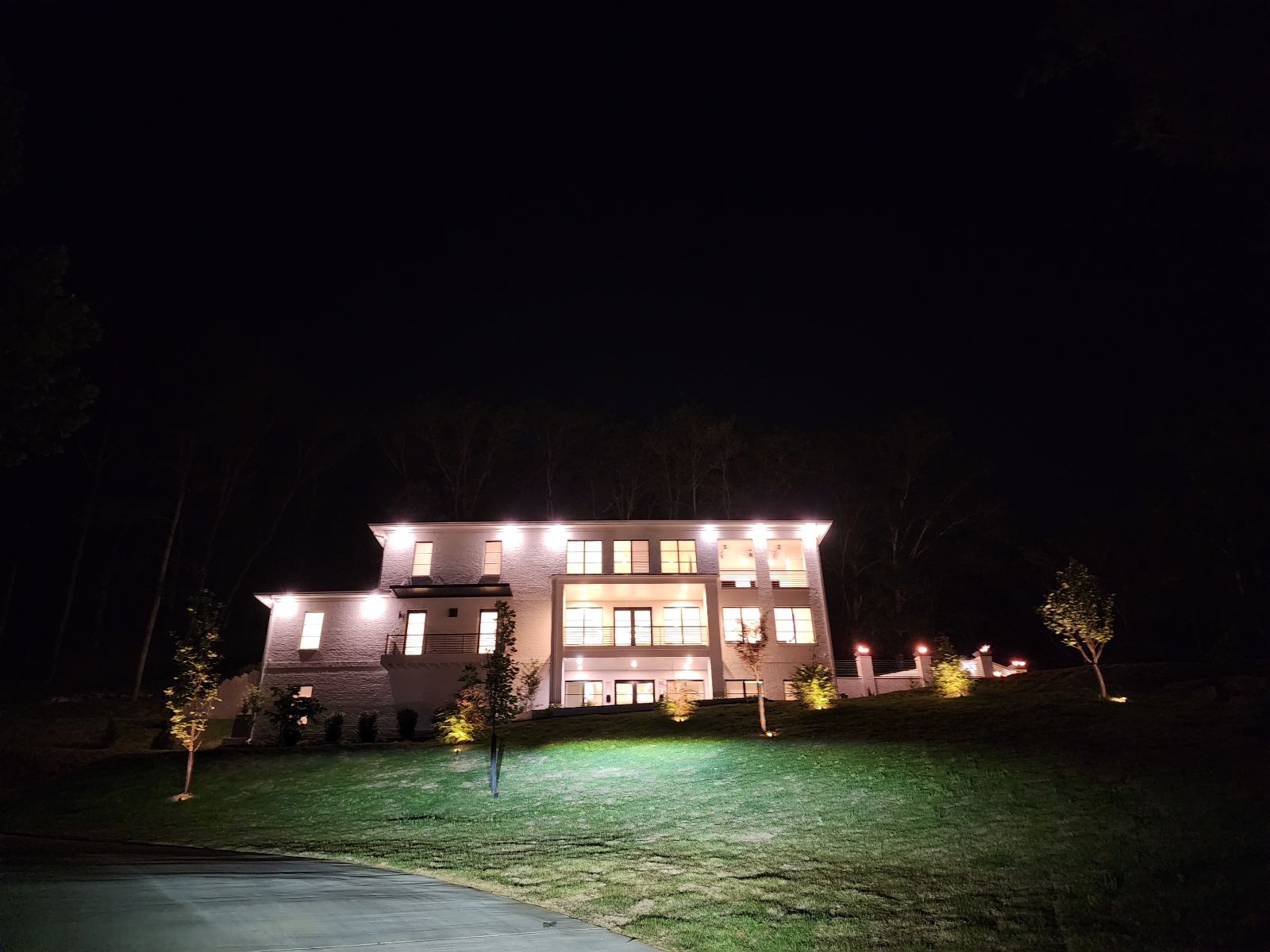 Large custom home illuminated at night with landscaped lawn and wooded surroundings