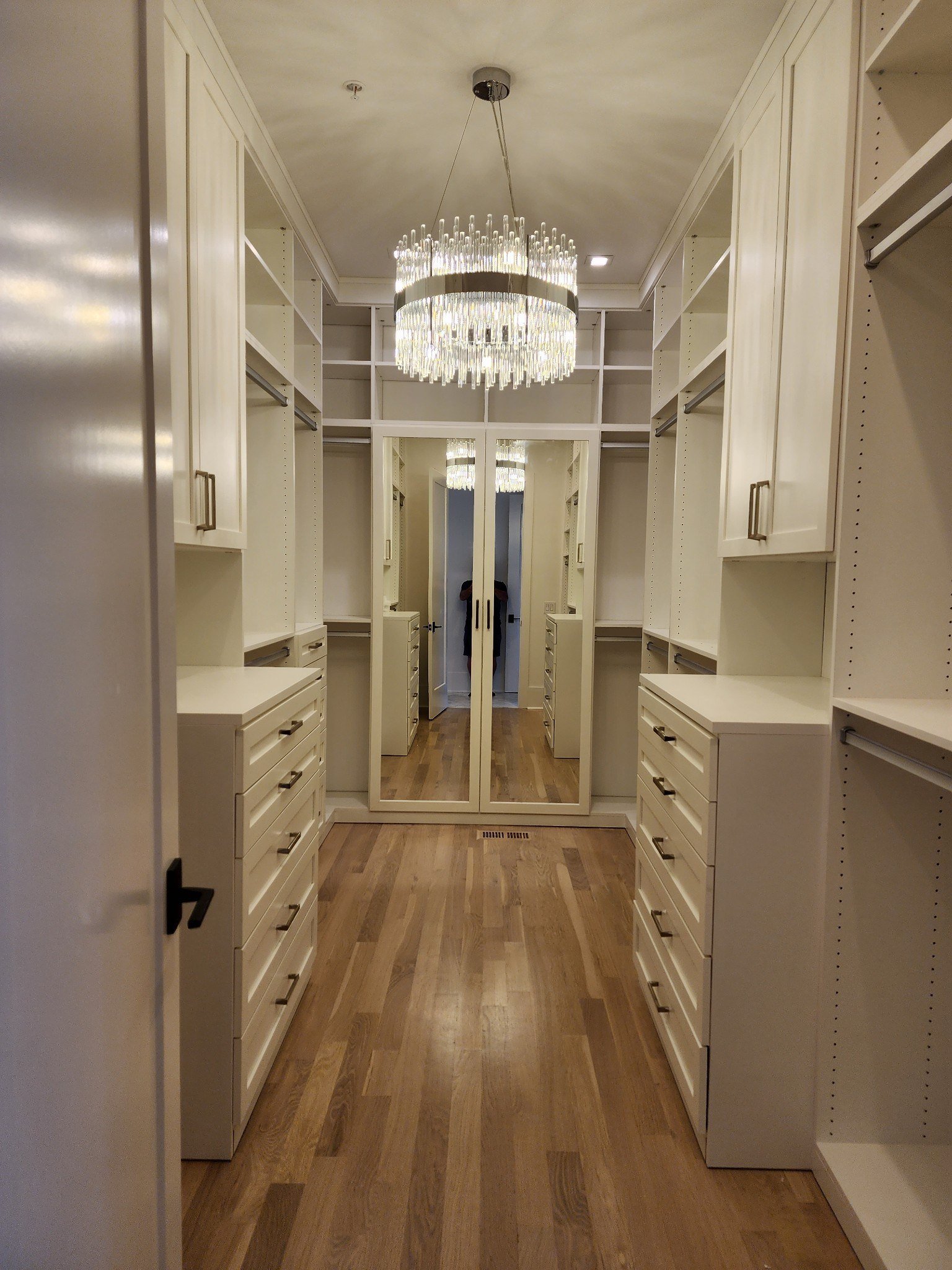 Finished walk-in closet with custom cabinetry, mirrored storage, hardwood floors, and chandelier