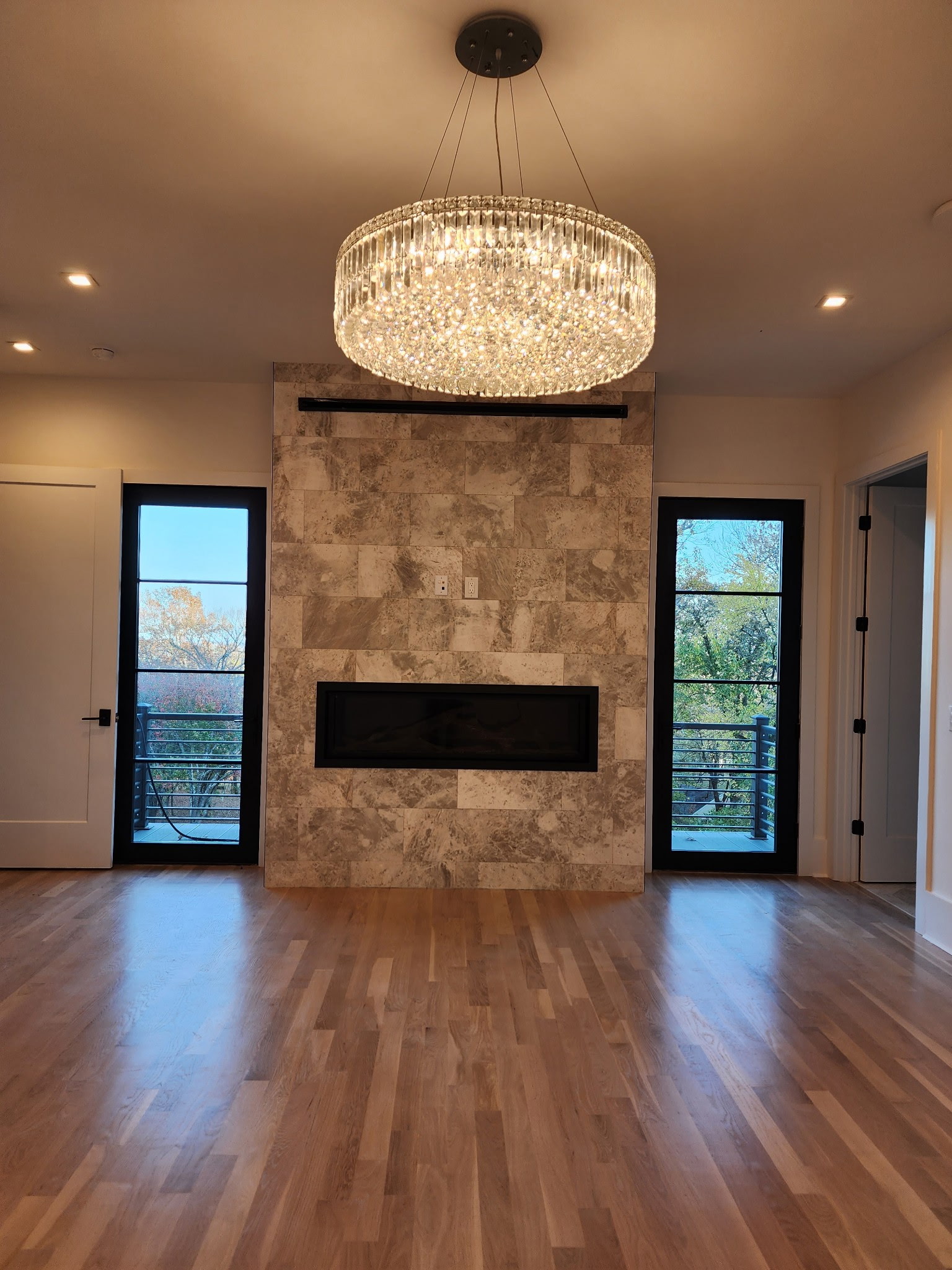 Finished custom interior with hardwood floors, a stone fireplace, crystal chandelier, and black-framed doors