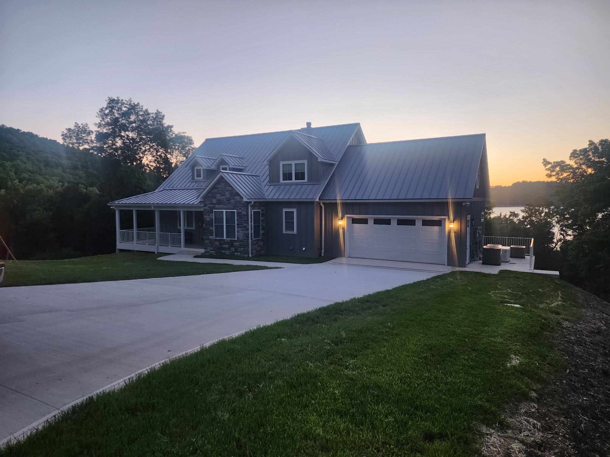 Completed custom home with a metal roof overlooking the lake at sunset