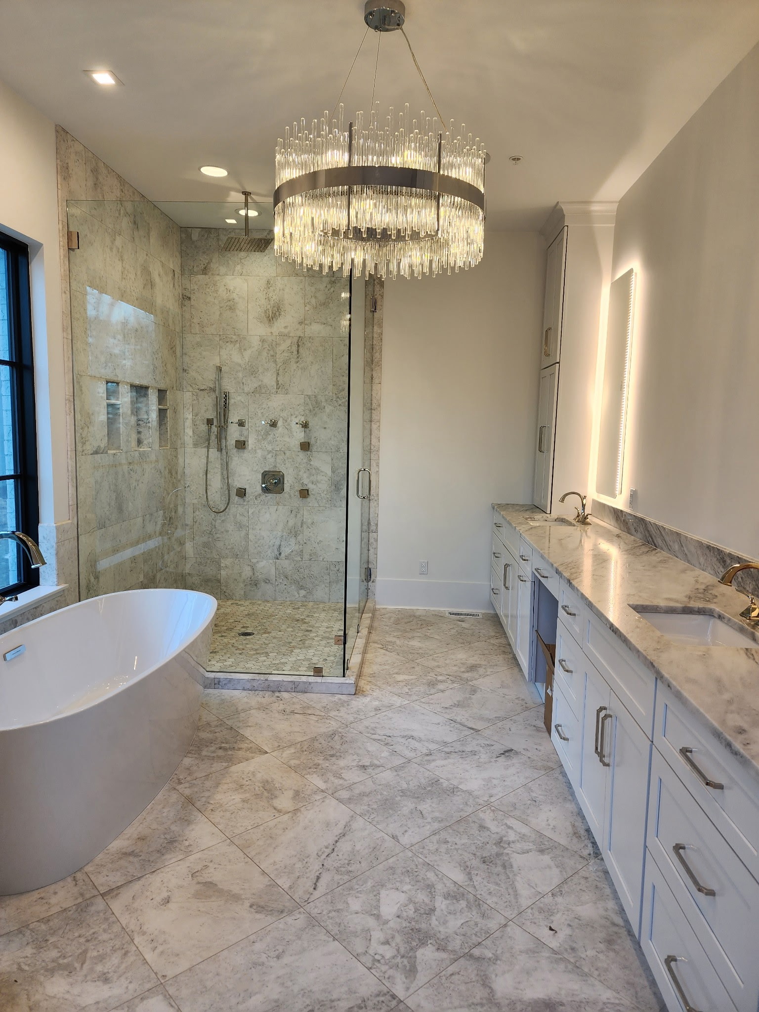 Luxury primary bathroom with a freestanding tub, glass shower, crystal chandelier, and custom vanity