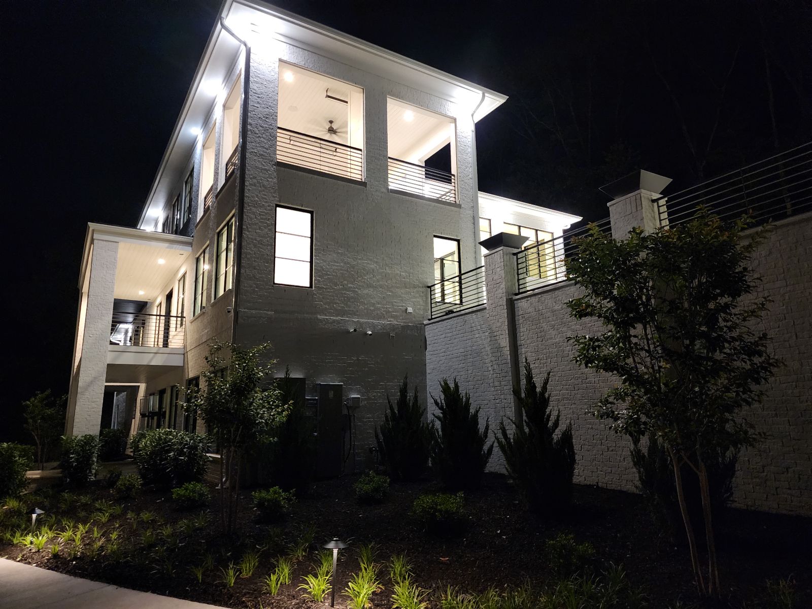 Modern white custom home illuminated at night with covered balconies and landscaped grounds